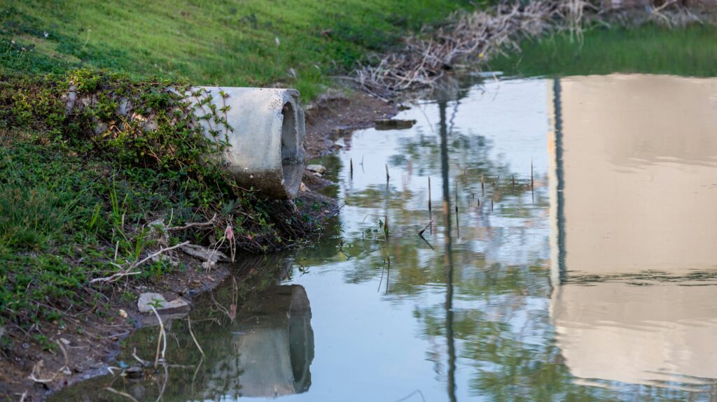 Concrete circular run-off pipe discharging water. sewage pipe polluting the river.